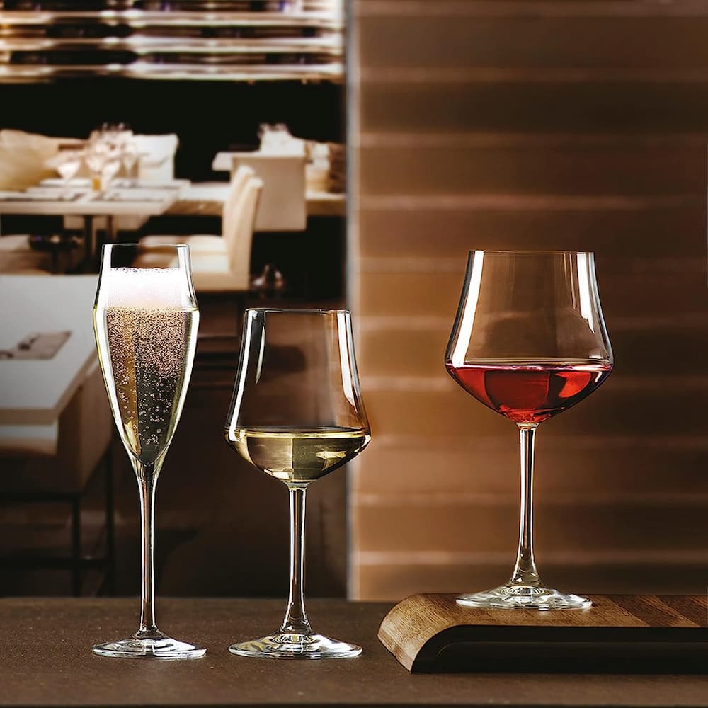 Колекция кристални чаши EGO - чаша със шампанско, чаша с бяло вино и чаша с червено вино върху дървена поставка на елегантна маса в елегантен ресторант.