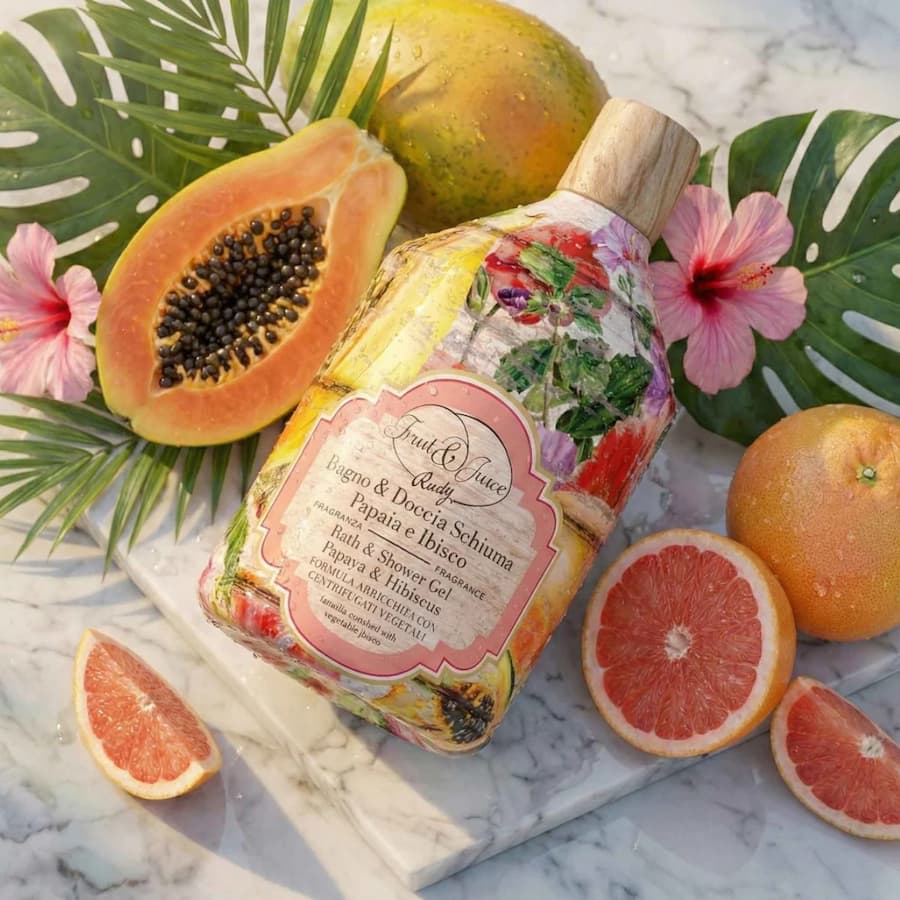 Душ гел Rudy Profumi Fruit & Juice Папая и хибискус 500 мл върху мраморен плот със резени тропически плодове и тропически листа и цветя около бутилката, за истинско лятно настроение и свежо усещане върху кожата с тропически аромат.