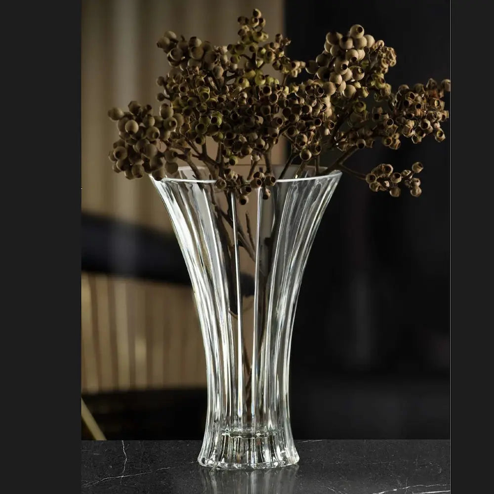 Кристална ваза поставена върху елегантен черно мраморен плот, изпълнена със клони с дребни плодове, с нежен черно златист фон, с лека светлина. Подходяща за високостъблени цветя и средно големи букети, стабилна, елегантна, Вписва се във всеки интериорен контекст. Идеален подарък за нов дом