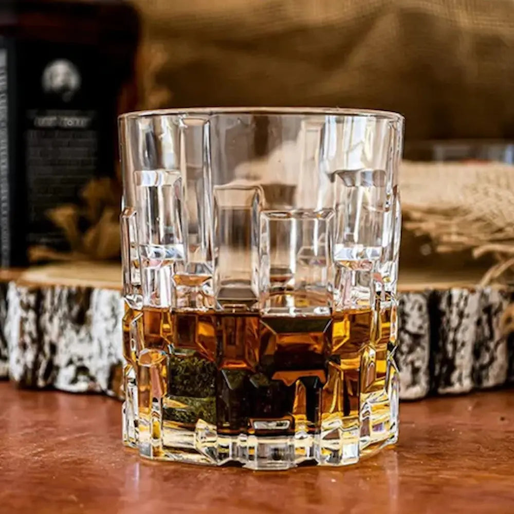 Eлегантна кристална чаша Етна с налято уиски, поставена върху вървена маса, в заден фон дървена поставка с бутилка пълна с уиски и опаковка от юта.