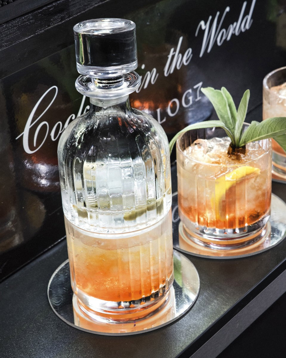 Елегантен комплект за уиски от 3 части - 2 бр. чаши от кристал Luxion с направени коктейли в тях + Гарафа сложена върху първата чаша в обстановка на бар.