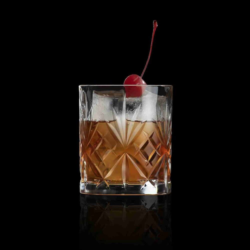 Елегантна кристална чаша MELODIA с класически диамантен декор, пълна с уиски коктейл, ледени кубчета и червена череша в близък план на черен фон