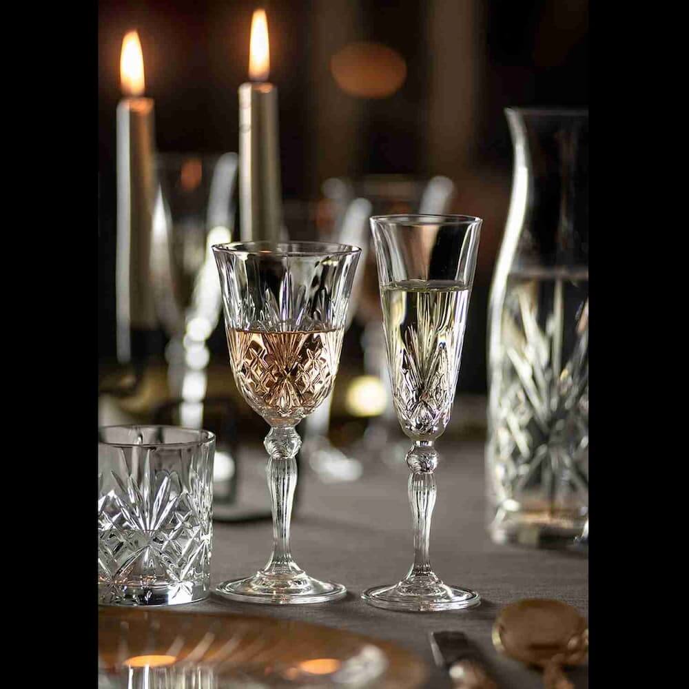Колекция кристални чаши MELODIA RCR с брилянтен гравиран дизайн в романтична обстановка със свещи на елегантна маса.